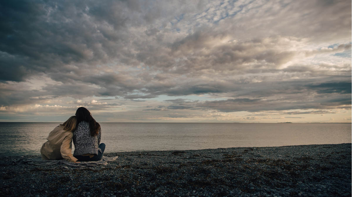 Person sitter på strand vid havet med utsikt över horisont och molnig himmel