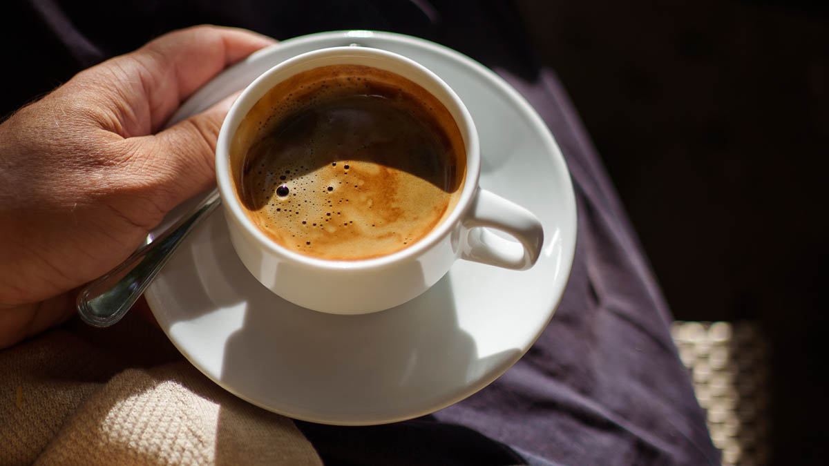 Espresso i vit kopp och fat som hålls i handen, med crema på ytan och kaffesked vid sidan