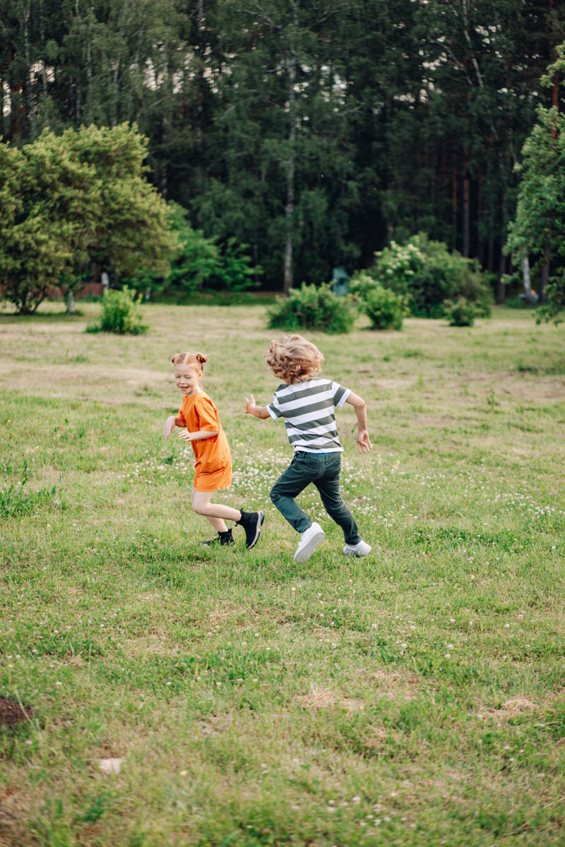 Två barn springer över en gräsyta med skog i bakgrunden