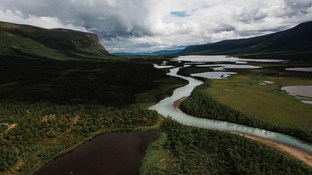 Slingrande flod genom grön dal med berg och molnigt landskap