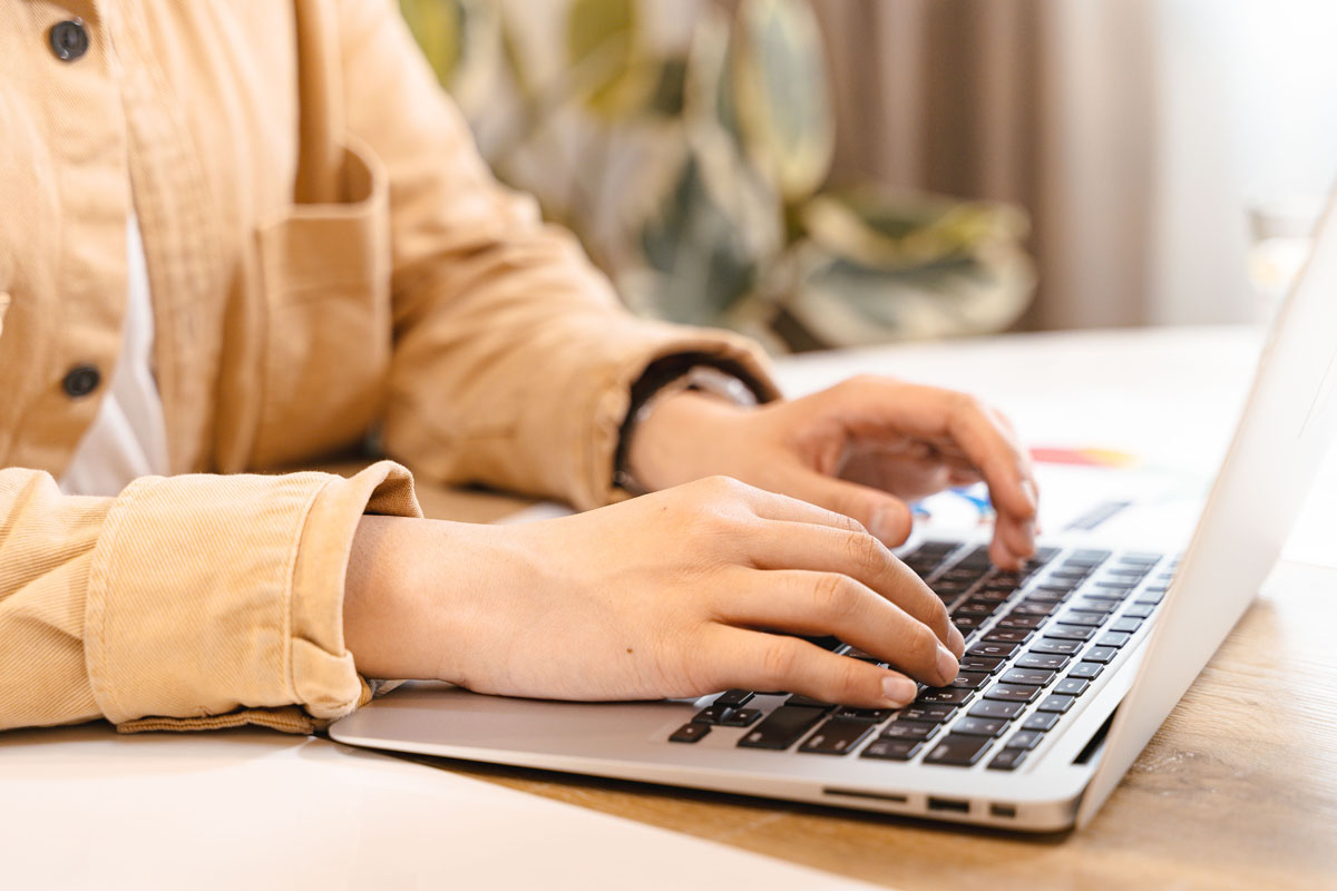 Händer som skriver på laptop i hemmiljö med växt i bakgrunden