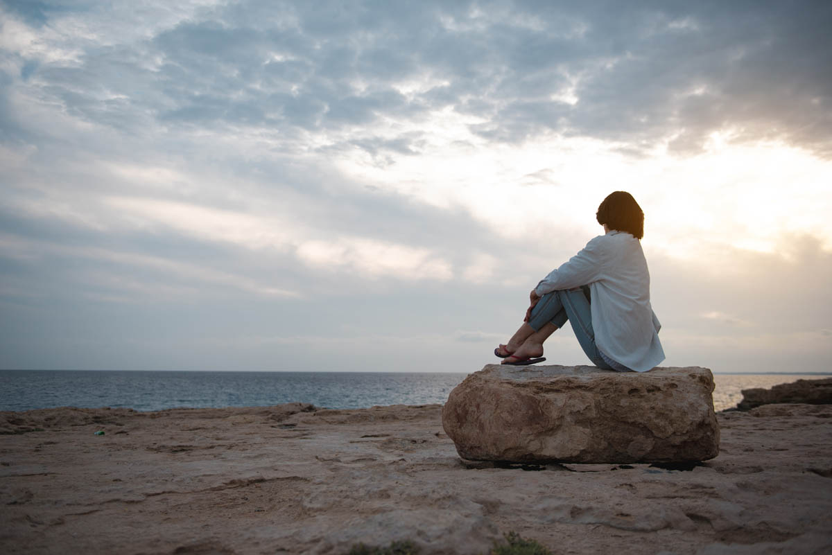 Person sitter vid havet och ser ut över vattnet